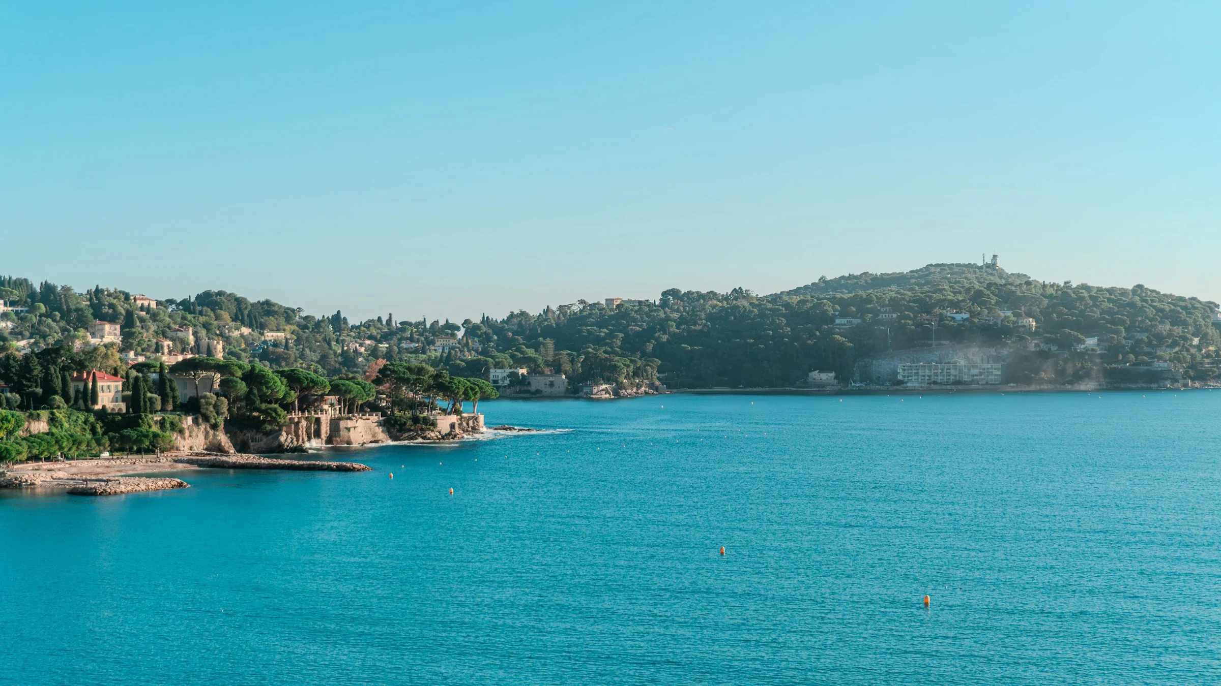 Turquoise water in the bay of Villefranche-sur-Mer, with the wooded Cap Ferrat peninsula under clear skies