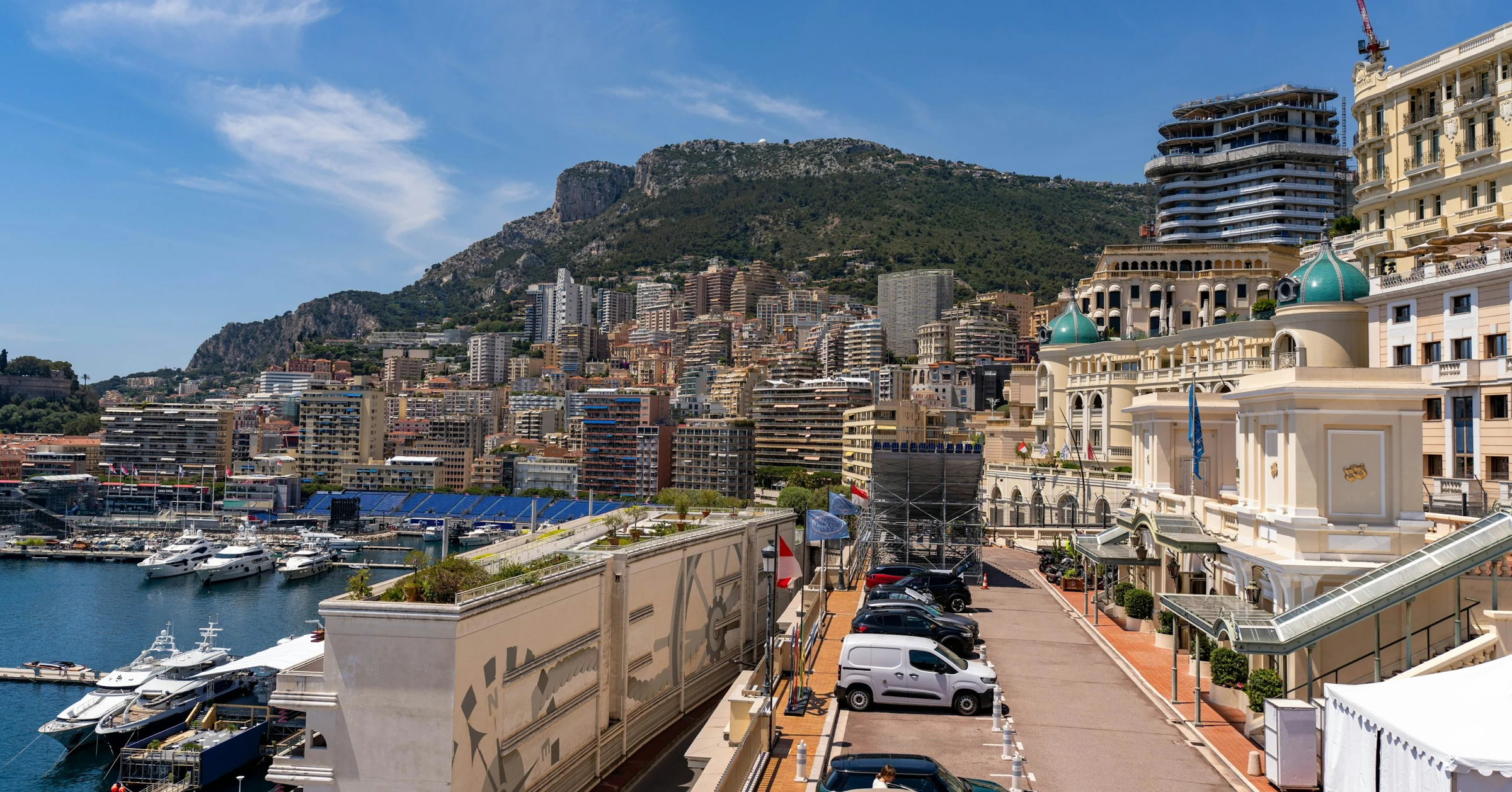 Yachts in Monaco’s Port Hercule below the city and mountains on a sunny day