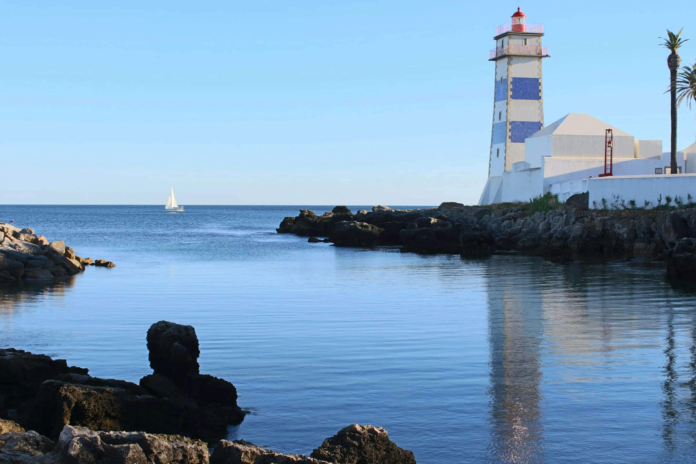 Blue-and-white Santa Marta Lighthouse beside calm coastal water in Cascais